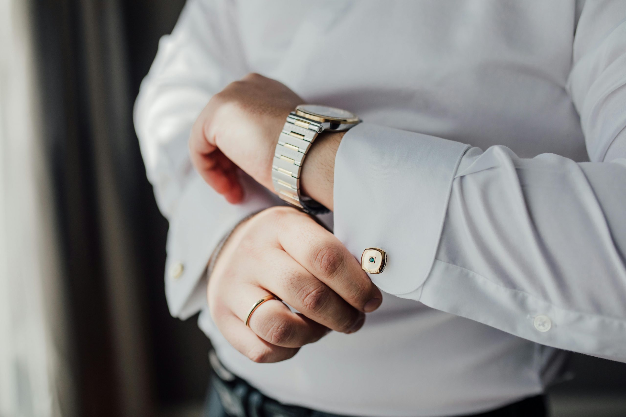 Close-up of a man adjusting his shirt cufflink, wearing a watch and wedding ring.