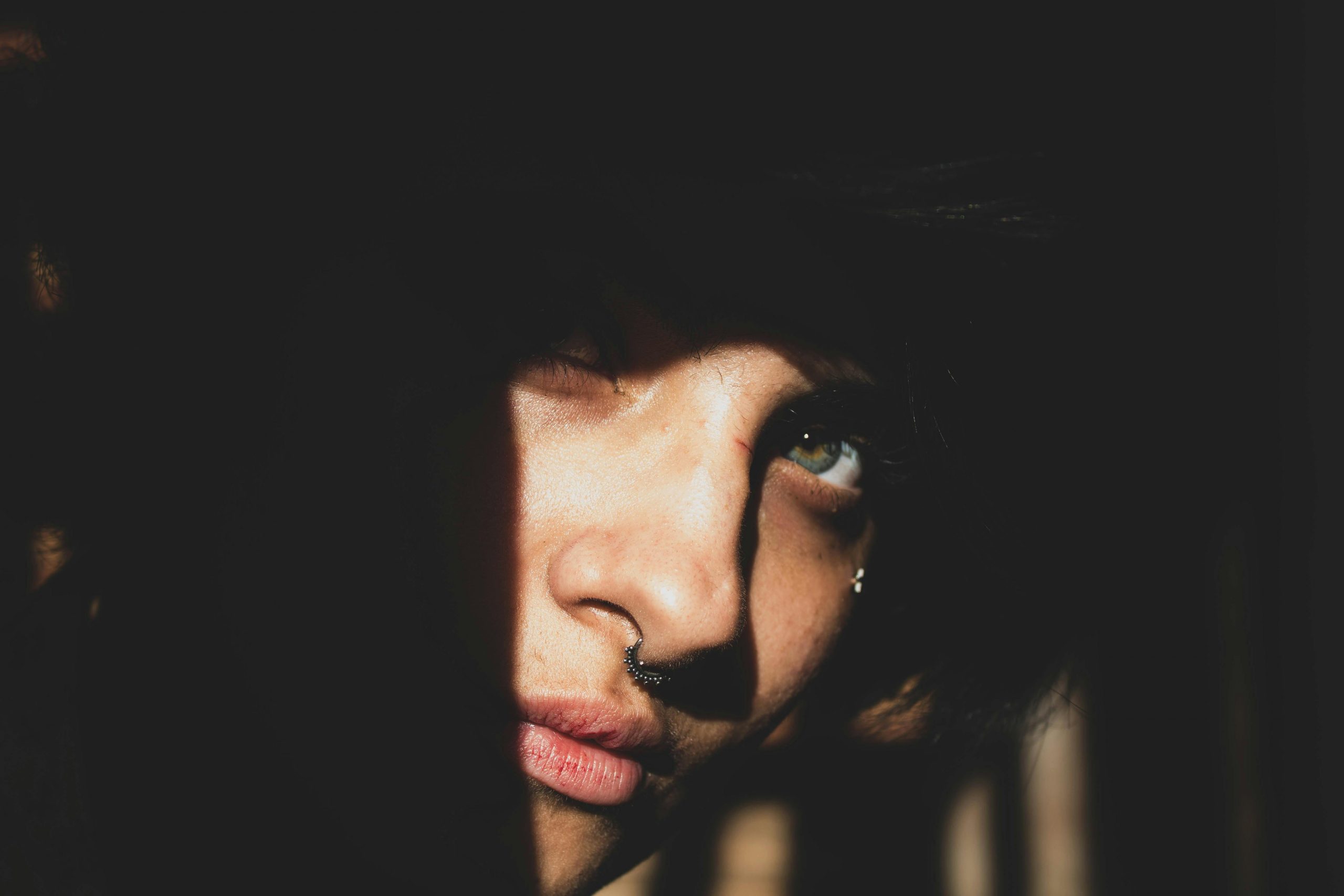 Captivating portrait highlighting face with shadows and nose piercing.