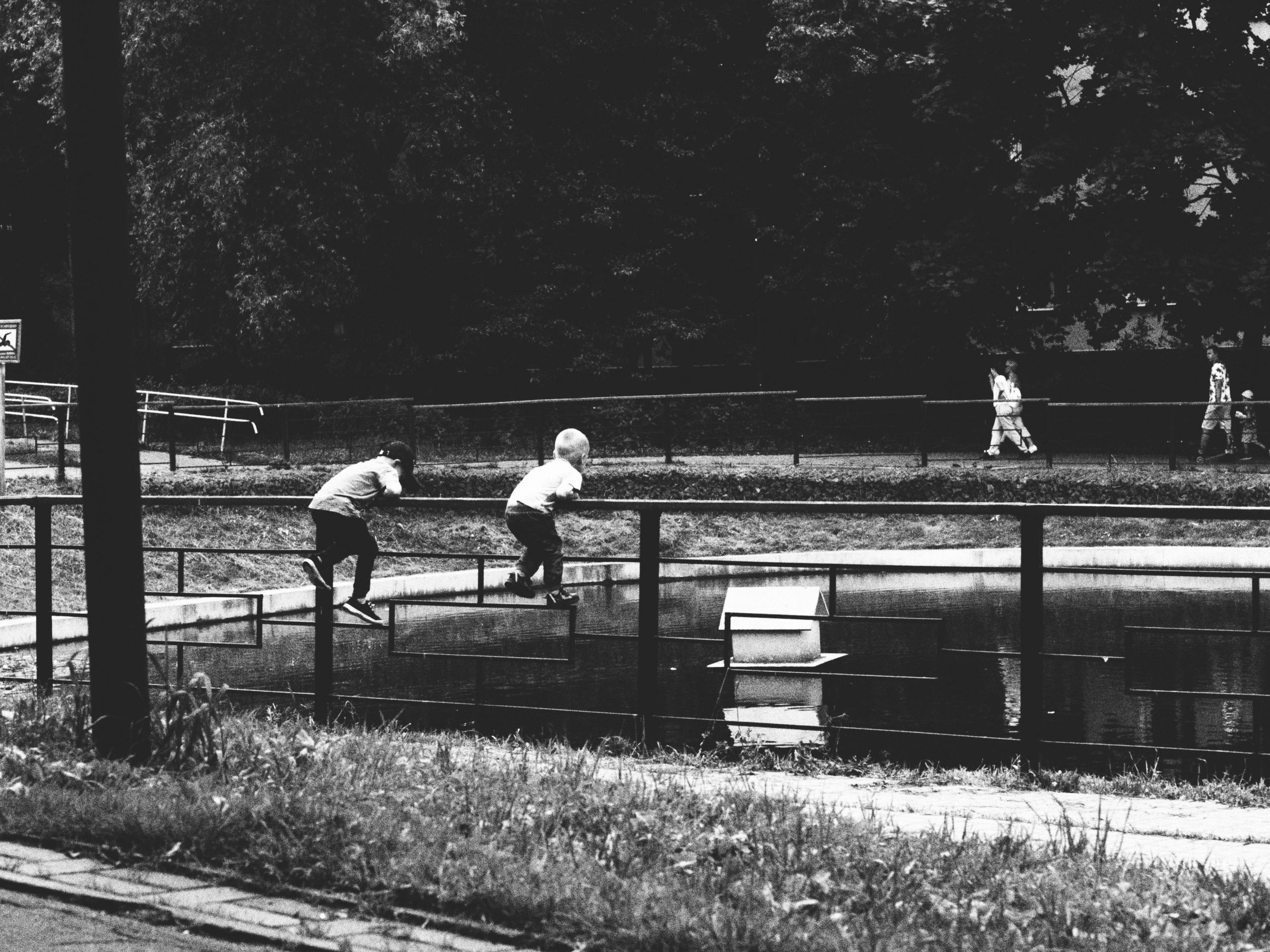 Black and white image of children playing near a pond in an urban park.